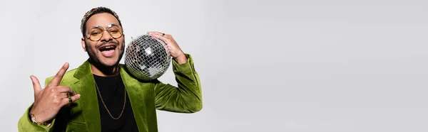 Збуджений індійський хіп-хоп виконавець в зеленому оксамитовому блістері і корона тримає диско м'яч ізольовано на сірому, банер — стокове фото
