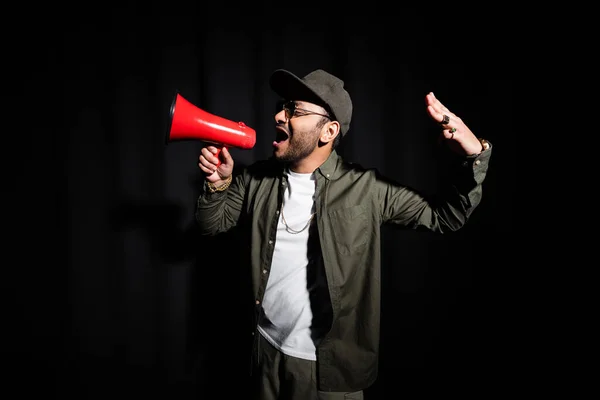 Émotionnel Moyen-Orient hip hop chanteur dans des lunettes de soleil parler en haut-parleur sur noir — Photo de stock