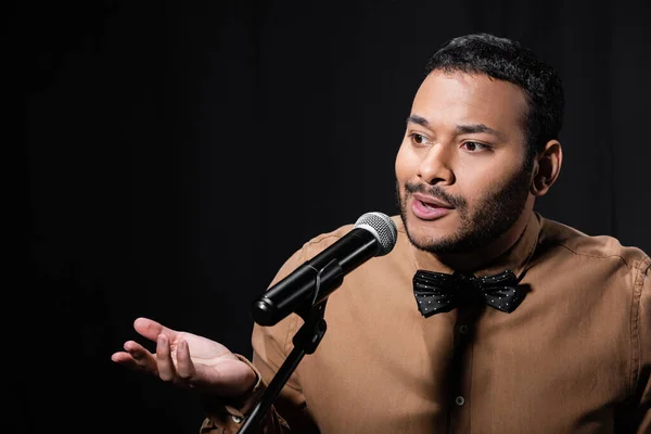 Confused eastern stand up comedian telling jokes into microphone on stand isolated on black — Fotografia de Stock