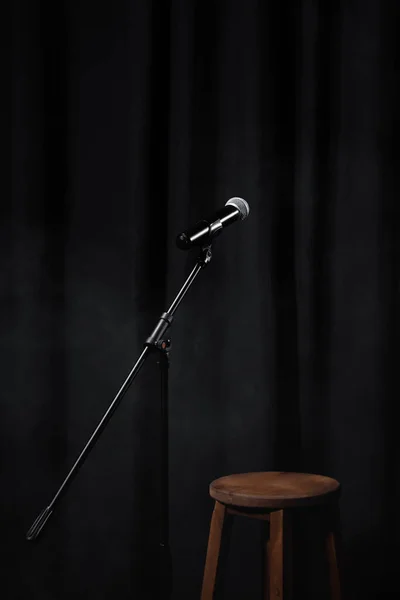 Microphone on stand on black stage with curtain and wooden chair — Stock Photo