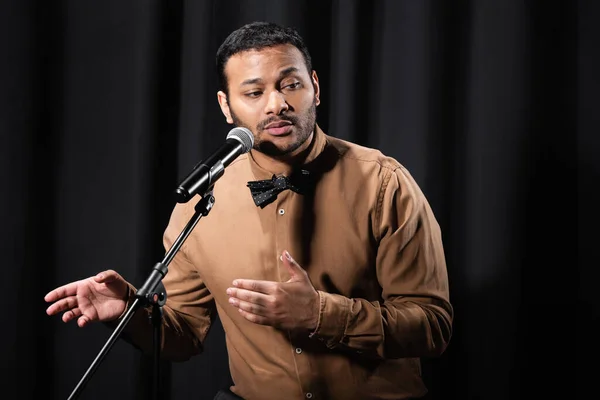 Indian comedian performing stand up comedy and telling jokes in microphone on black stage — Stock Photo