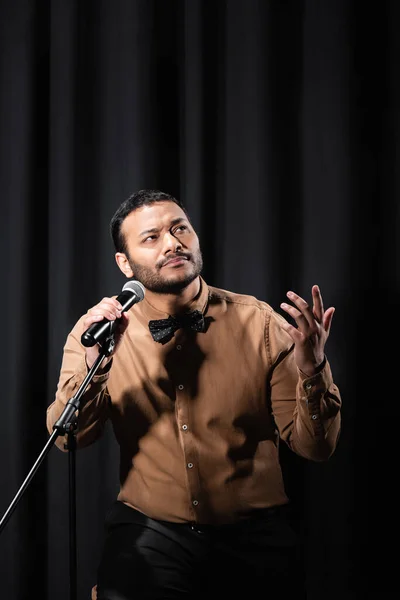 Pensive indian comedian performing stand up comedy and telling jokes in microphone on black — Photo de stock