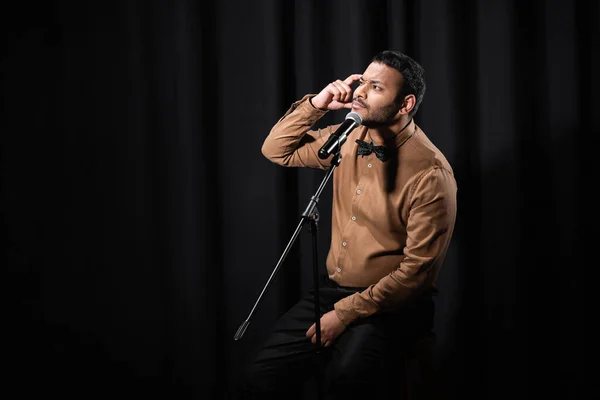 Thoughtful indian comedian performing stand up comedy and telling jokes in microphone on black — Stock Photo