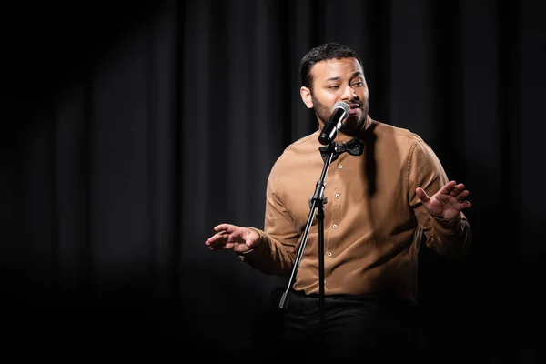 Indian comedian gesturing and performing stand up comedy while telling jokes in microphone on black — Stock Photo