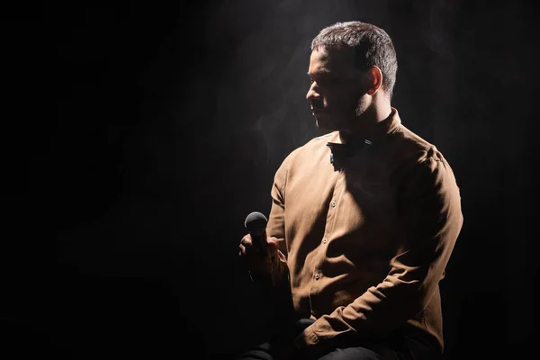 Indian stand up comedian holding microphone and looking away on black with smoke — Fotografia de Stock