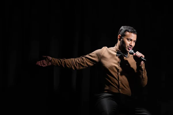 Eastern comedian sitting and performing stand up comedy into microphone on black — Foto stock