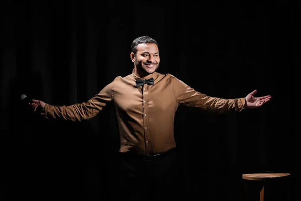 Feliz comediante do Oriente Médio gesto e segurando microfone no preto — Fotografia de Stock