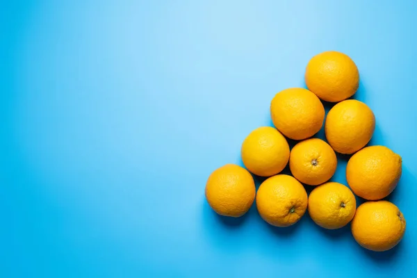 Flat lay with fresh oranges in triangle shape on blue background — Fotografia de Stock