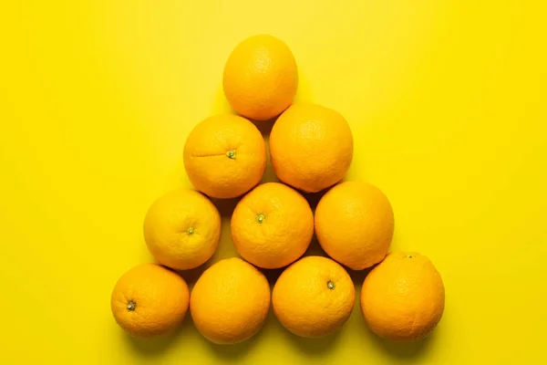 Colocación plana con naranjas en forma de triángulo sobre fondo amarillo - foto de stock