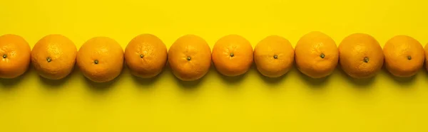 Pose plate avec des mandarines en rangée sur fond jaune, bannière — Photo de stock