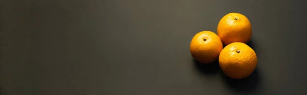 Vista de ángulo alto de sabrosas mandarinas en la superficie negra, bandera - foto de stock