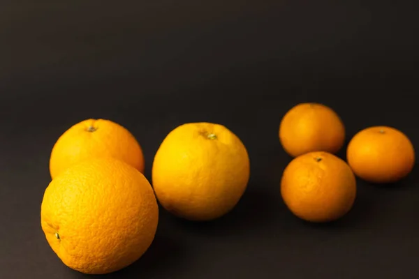 Свежие апельсины рядом с размытыми мандаринами на черном фоне — стоковое фото