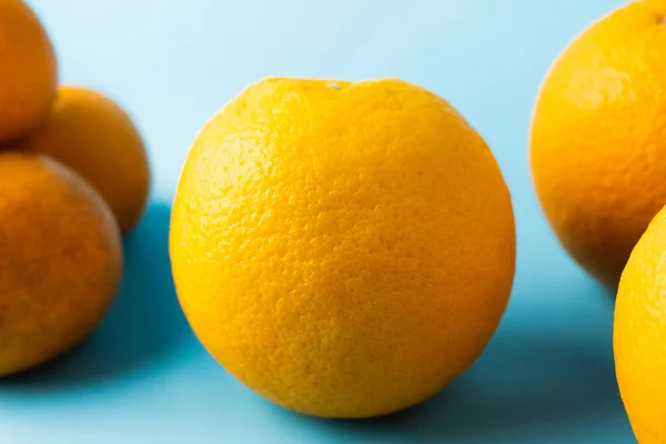 Vista cercana de naranjas cerca de mandarinas borrosas en la superficie azul - foto de stock