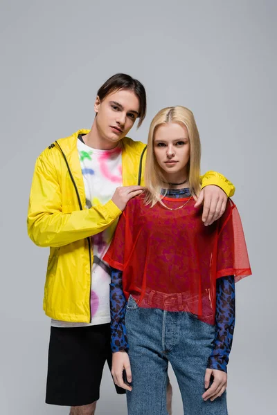 Young man in windbreaker hugging blonde girlfriend isolated on grey — Stock Photo