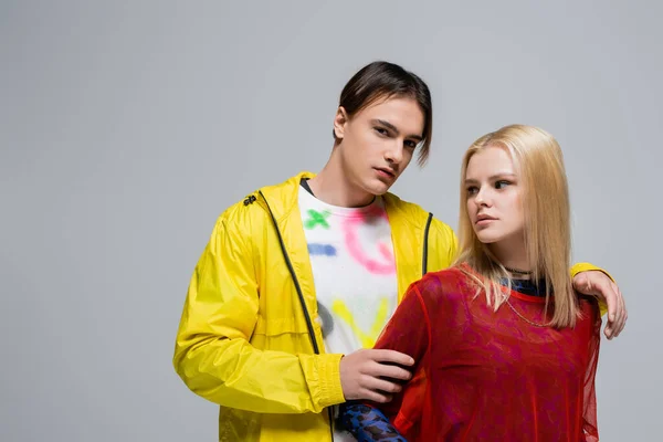 Man in yellow windbreaker hugging girlfriend and looking at camera isolated on grey — Fotografia de Stock