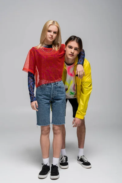 Jeune femme en short en denim étreignant son petit ami sur fond gris — Photo de stock