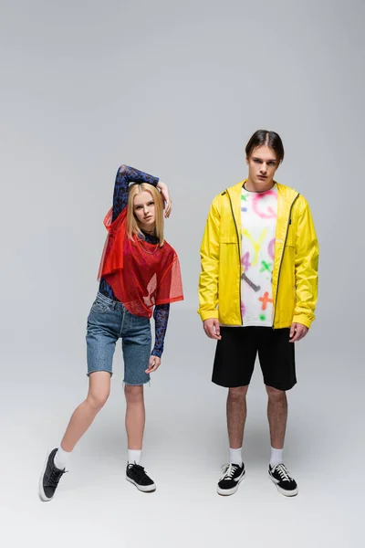 Full length of trendy couple in bright clothes posing on grey background — Photo de stock