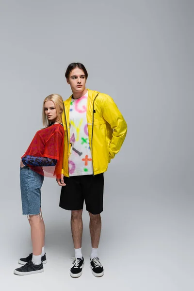 Stylish woman standing near boyfriend in windbreaker and shorts on grey background — Stock Photo