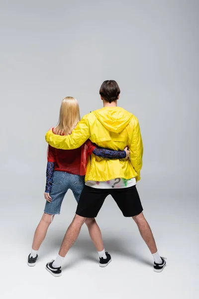 Vista trasera de la joven pareja de moda abrazándose sobre fondo gris - foto de stock
