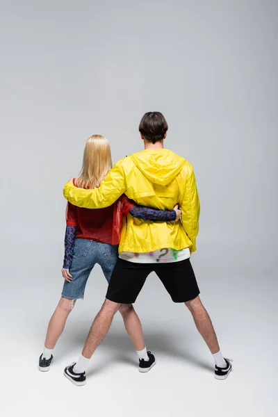 Back view of young trendy couple hugging on grey background — Stock Photo