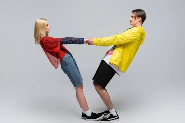 Seitenansicht eines jungen Paares in trendiger Kleidung, das Händchen haltend auf grauem Hintergrund — Stockfoto