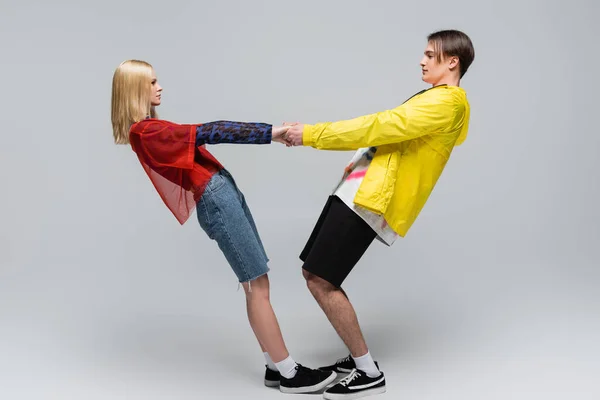 Side view of young couple in trendy clothes holding hands on grey background — Stock Photo