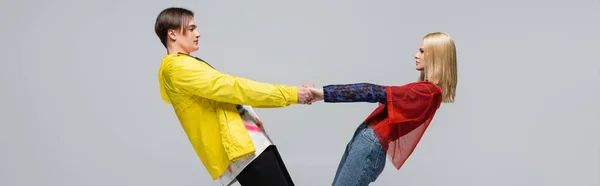 Side view of young couple in bright clothes holding hands isolated on grey, banner — Stockfoto