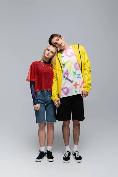 Full length of stylish young couple holding hands and looking at camera on grey background — Photo de stock