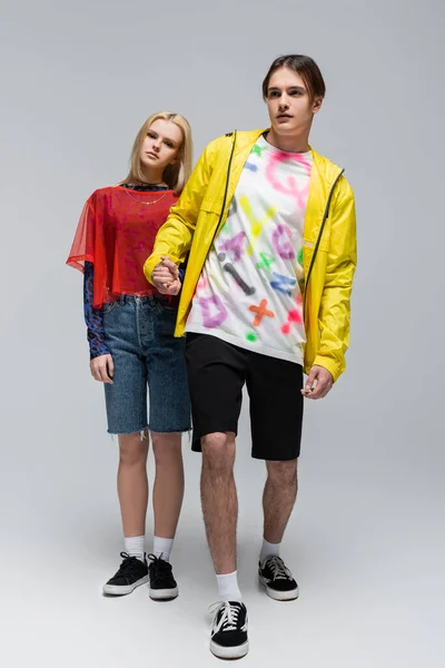 Full length of stylish man in windbreaker holding hand of girlfriend on grey background — Foto stock