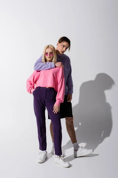 Stylish man hugging girlfriend in sunglasses on grey background — Fotografia de Stock