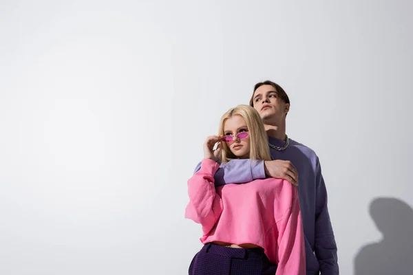 Мужчина в фиолетовой толстовке обнимает девушку в солнечных очках на сером фоне — стоковое фото