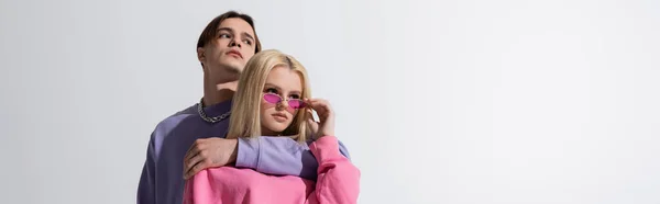 Giovane uomo che abbraccia la ragazza bionda in occhiali da sole rosa isolati su grigio, banner — Foto stock