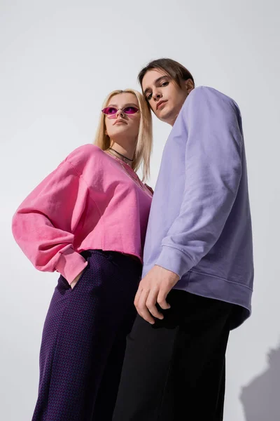 Low angle view of fashionable young couple posing on grey background — Stockfoto