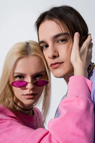 Portrait of blonde woman in pink sunglasses touching boyfriend isolated on grey — Foto stock