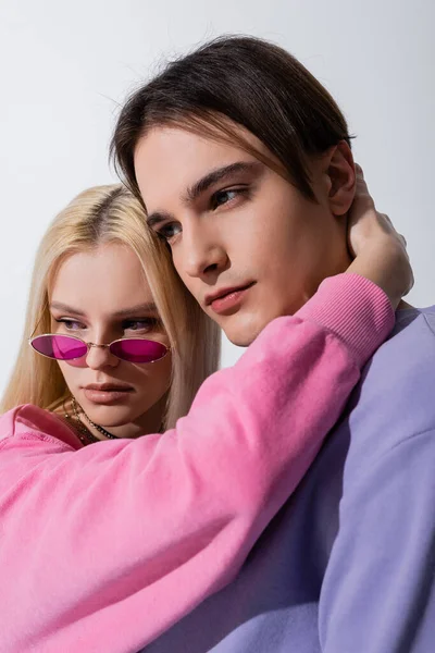 Joven mujer rubia en gafas de sol abrazando novio aislado en gris - foto de stock