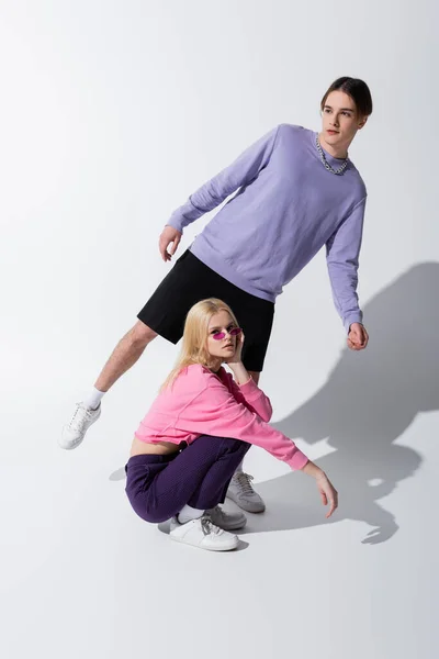 Young blonde woman in sunglasses looking at camera near boyfriend on grey background - foto de stock