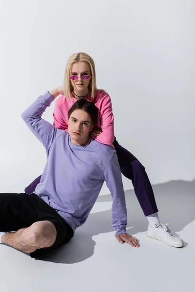 Stilvolles Paar in Sweatshirts blickt in die Kamera, während es auf grauem Hintergrund posiert — Stockfoto