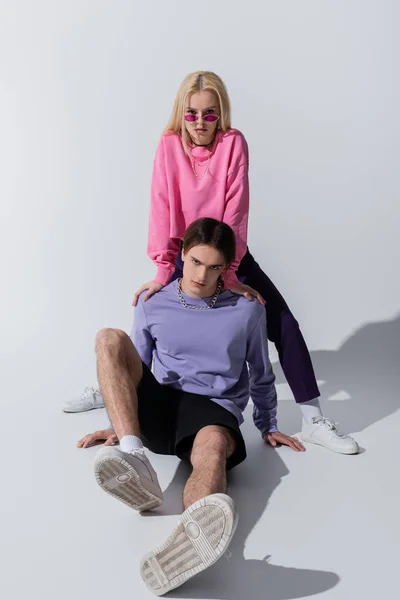 Pareja joven en sudaderas y zapatillas posando sobre fondo gris - foto de stock