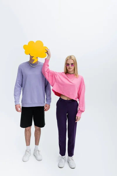 Stylish model in sunglasses holding thought bubble near boyfriend on grey background — Foto stock