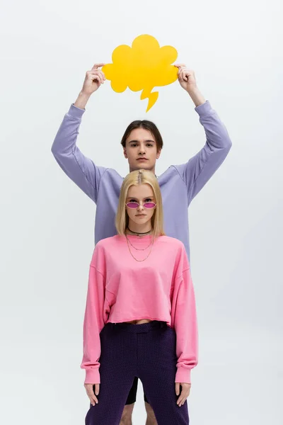 Brunette man holding thought bubble above girlfriend in sunglasses and sweatshirt isolated on grey — Fotografia de Stock