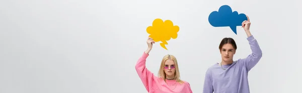 Young couple in sweatshirts holding thought bubbles isolated on grey, banner - foto de stock