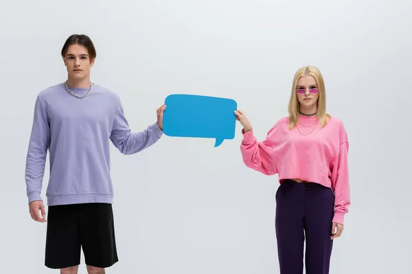 Stylish young couple in sweatshirts holding speech bubble isolated on grey — Fotografia de Stock