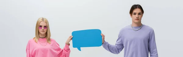 Young couple in sweatshirts holding speech bubble isolated on grey, banner - foto de stock