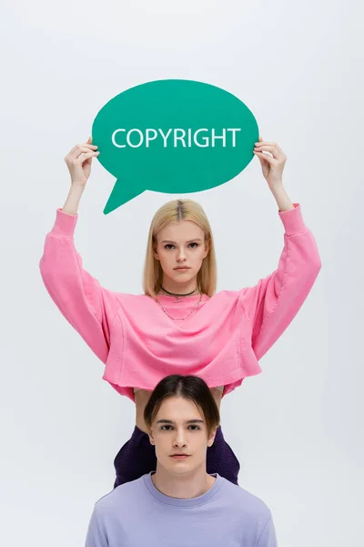 Stylish blonde woman holding speech bubble with copyright lettering near boyfriend isolated on grey — Stock Photo