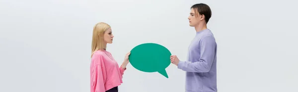 Side view of man and woman in sweatshirts holding speech bubble isolated on grey, banner — Foto stock