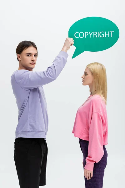 Young man holding speech bubble with copyright lettering near girlfriend isolated on grey — Stock Photo