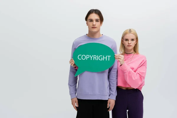 Junge Frau im Sweatshirt hält Sprechblase mit Urheberrechtsaufdruck isoliert auf grau — Stockfoto
