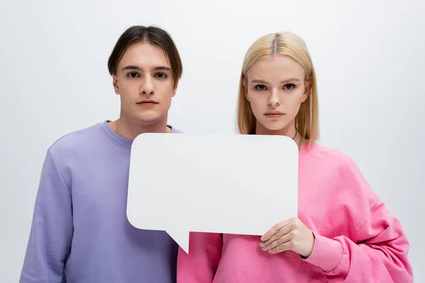 Junges Paar in Sweatshirts mit weißer Sprechblase isoliert auf grau — Stockfoto