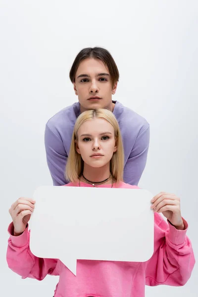 Brunette man looking at camera near girlfriend with white speech bubble isolated on grey — Stockfoto