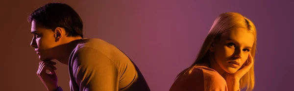 Блондинка смотрит в камеру рядом с парнем на фиолетовом фоне с освещением, баннером — стоковое фото